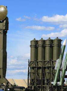 Military missile launcher array with green cylindrical tubes and supporting framework under a blue sky.